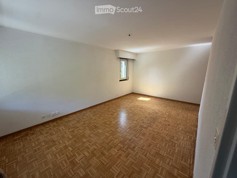 Empty room with wooden herringbone flooring, white walls, and a small window letting in natural light.