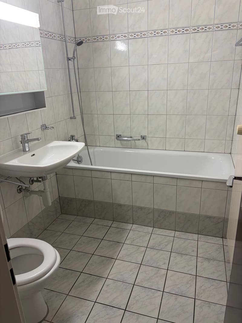 Bathroom with a toilet, bathtub, sink, and mirror. The walls are tiled with a decorative border, and the floor is tiled with marble-like tiles.