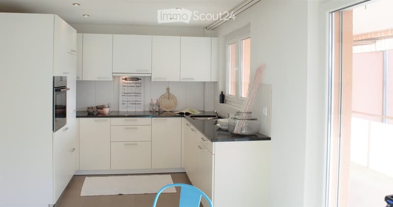Modern kitchen with white cabinets, black countertops, stainless steel sink, and various decorative items including a vase and a framed sign.