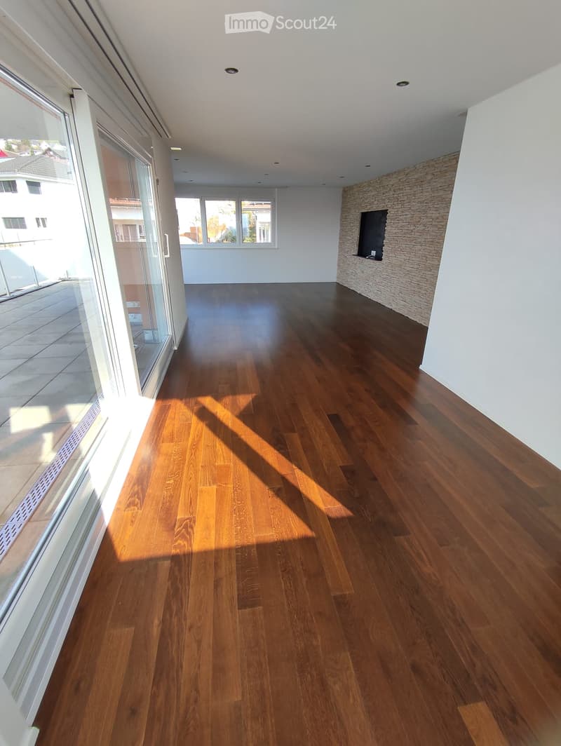 Empty room with polished wooden flooring, large windows, and a stone accent wall. No furniture or equipment present.