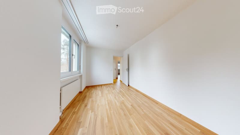 Empty room with light wooden flooring, white walls, and large windows. No furniture or equipment is present.