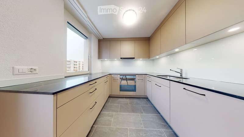 Modern kitchen with light-colored cabinets, glass countertop, and stainless steel sink.