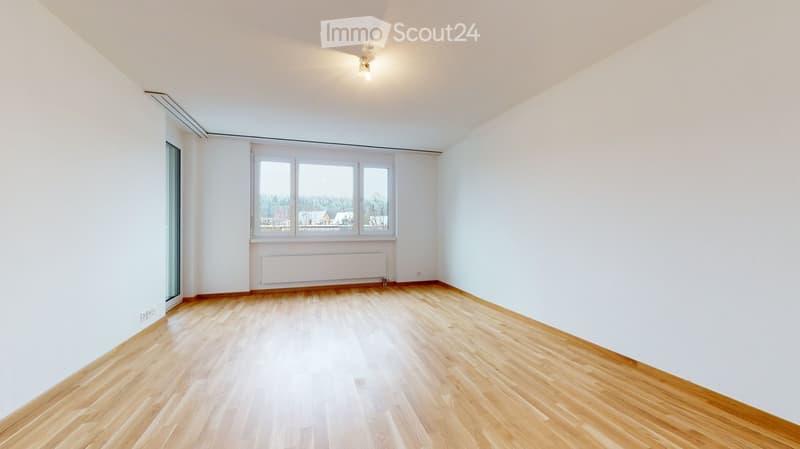 Empty room with light wooden flooring, white walls, and large windows offering a view of the outdoors.