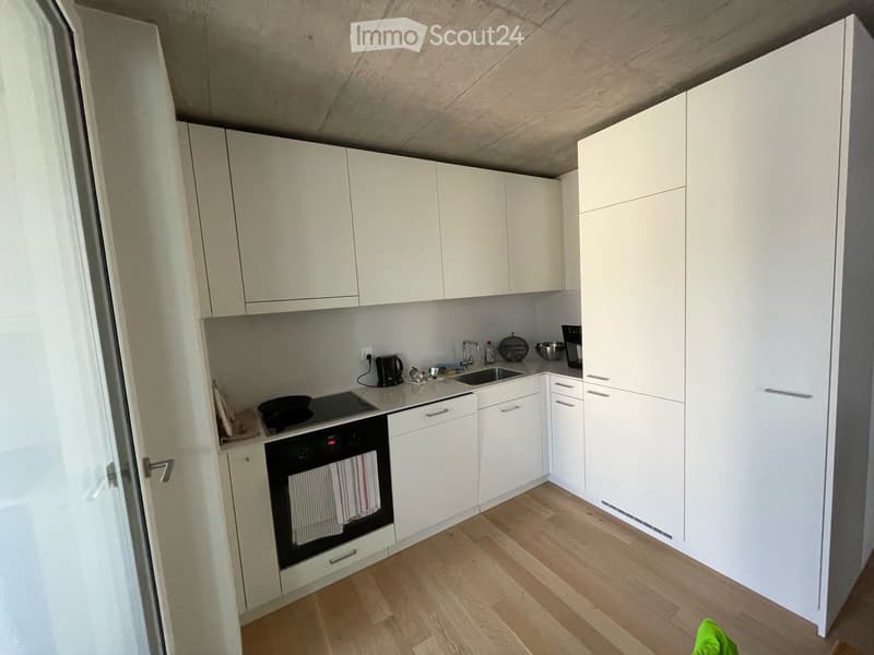 Modern kitchen with white cabinets, wooden flooring, and stainless steel appliances including an oven, sink, and coffee maker.