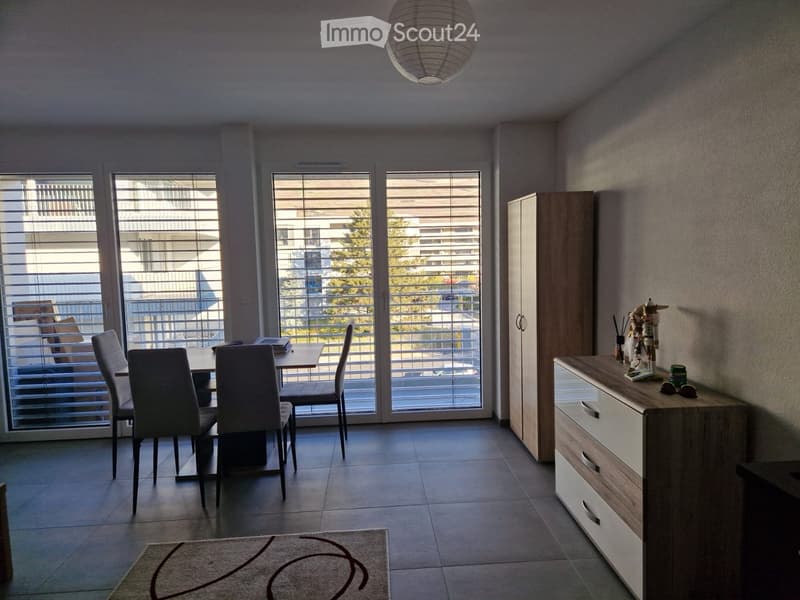 Furnished Room. Dining area with a table, chairs, a cabinet, and a drawer unit, featuring large windows with blinds and a view of the outside.