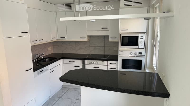 Modern kitchen with white cabinets, black countertops, and stainless steel appliances including a microwave, oven, and dishwasher.