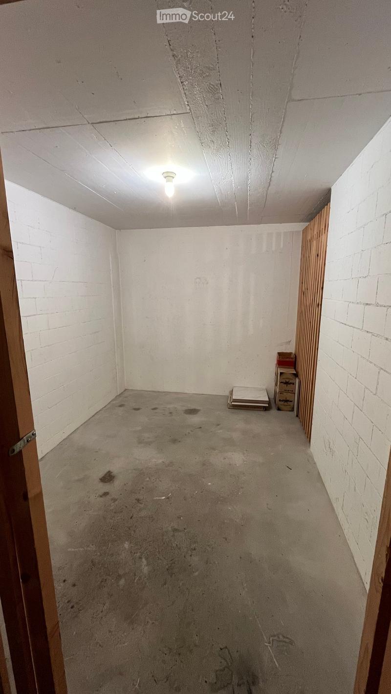 Empty room with white brick walls, concrete floor, and a single light fixture on the ceiling. There are a few boxes and a stack of papers in the corner.