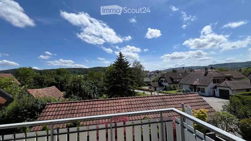 Balcony overlooking a residential neighborhood with houses, trees, and a clear blue sky.