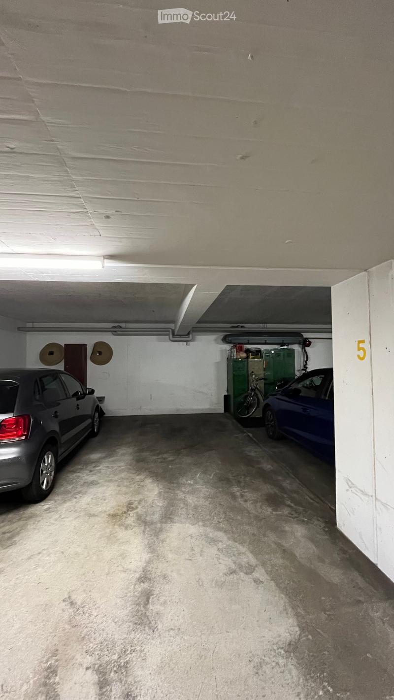 Underground parking area with two cars and a bicycle, concrete floor, white walls, and storage cabinets.