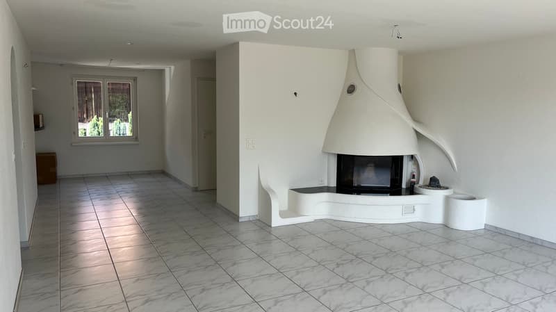 Modern living room with a white, sculptural fireplace, tiled floor, large window, and neutral-colored walls.