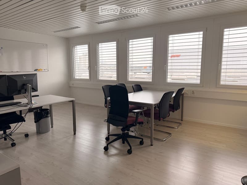 Spacious meeting room with wooden floor, large windows, whiteboard, table, and office chairs.