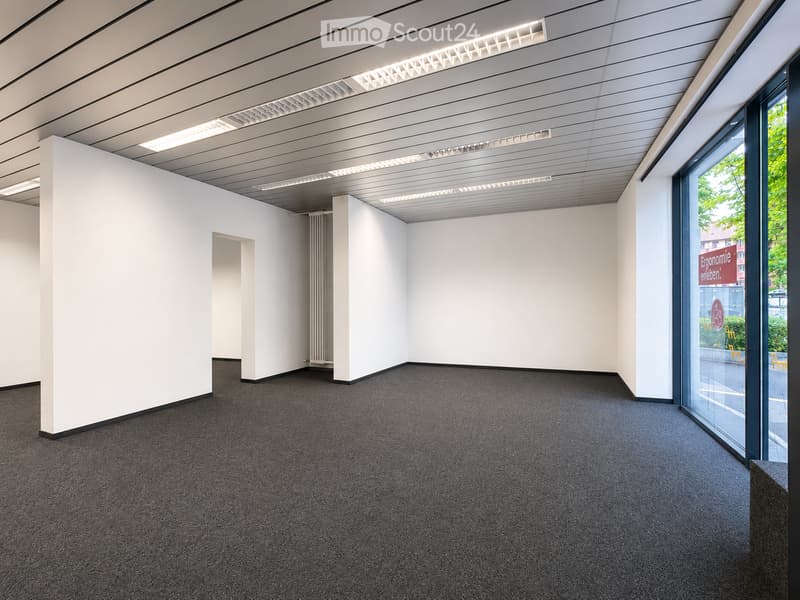 Empty room with white walls, grey carpeted floor, and large glass windows. No furniture or equipment present.