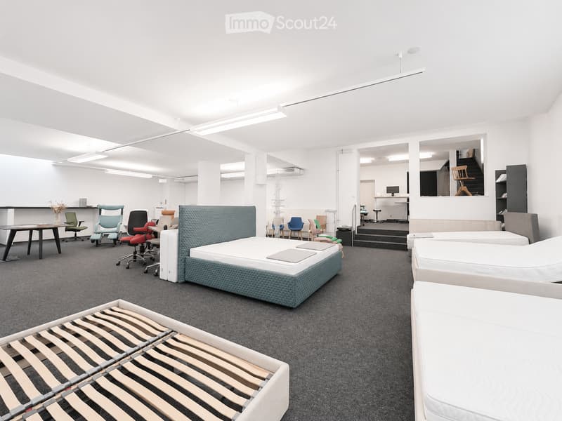 Modern showroom with multiple beds, chairs, tables, and a sofa, featuring a clean and organized layout with neutral tones and contemporary design.