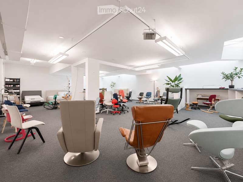 Modern, open-plan room with a variety of colorful chairs and stools, a small table, and plants, illuminated by bright overhead lighting.