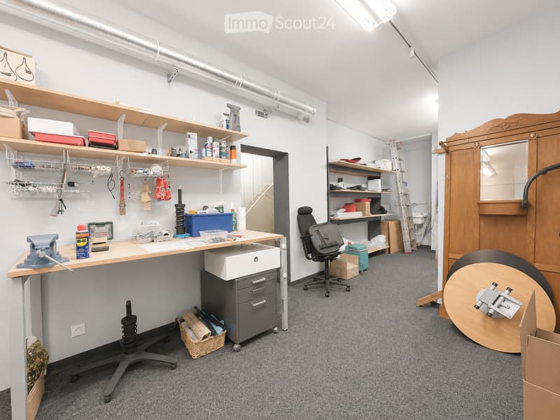 Well-organized workshop or studio space with a desk, chair, shelves filled with tools and supplies, a large wooden cabinet, and various equipment.