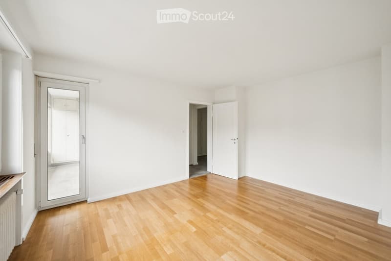 Empty room with light wooden flooring, white walls, and a large mirrored door leading to another space.