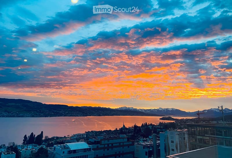 Balcony / Terrace. Panoramic view from a balcony or terrace overlooking a lake and cityscape at sunset, with mountains in the background.
