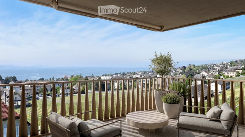 Balcony with a scenic view of a lake and town, featuring a round table, two chairs, and potted plants.