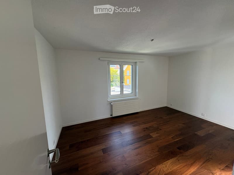 Empty room with wooden flooring, white walls, and a window with a radiator below it.