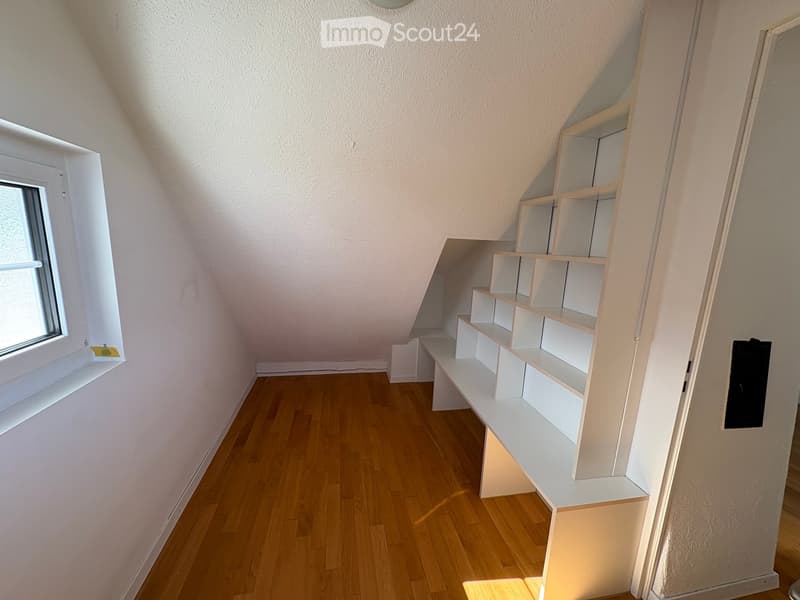 Empty room with wooden flooring, white walls, and built-in white shelving unit. A window on the left side allows natural light to enter.