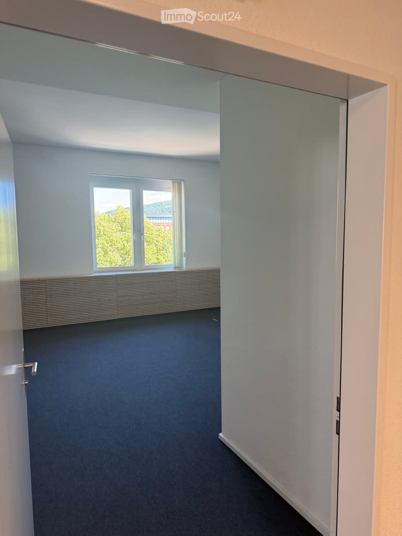 Empty room with grey carpeted floor, white walls, and a large window with blinds. No furniture or equipment present.