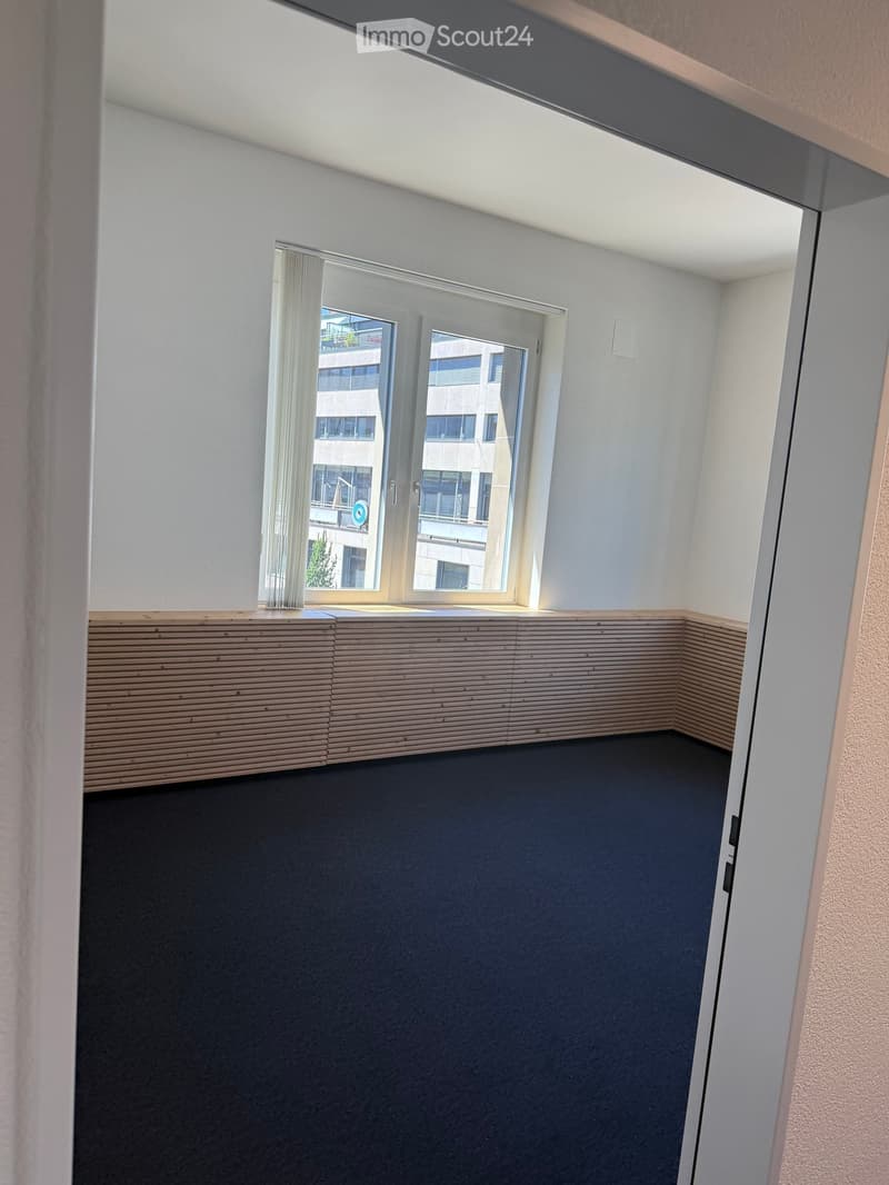 Empty room with dark flooring, light-colored walls, and a window with blinds. The room has a simple, modern design with no furniture or decorations.