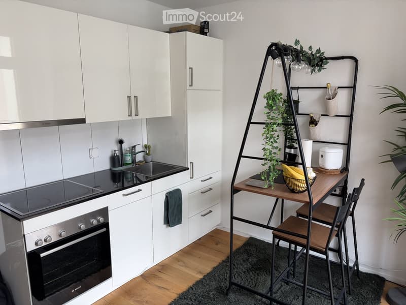 Modern kitchen with white cabinets, black countertop, sink, oven, and a small dining area with a table and chairs.