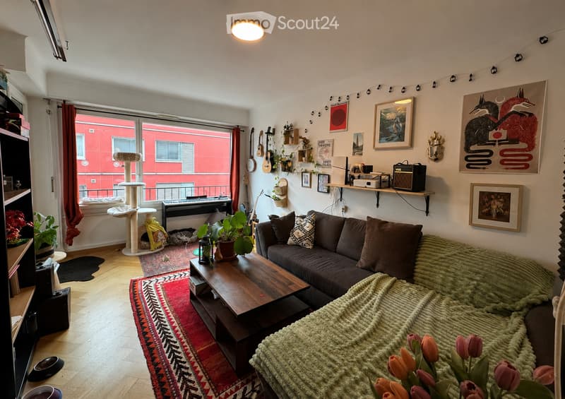 Cozy living room with a grey sectional sofa, wooden coffee table, cat tree, guitars, piano, and various decorative items including framed pictures and plants.