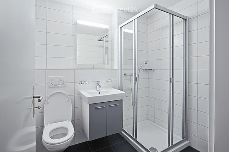 Modern bathroom with white tiles, a toilet, a sink with a mirror, and a glass-enclosed shower stall.