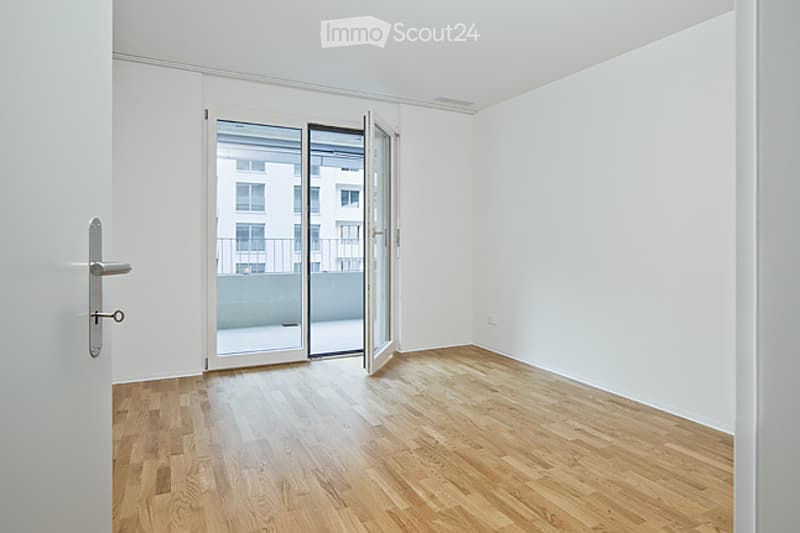 Empty room with wooden flooring, white walls, and a large sliding glass door leading to a balcony.