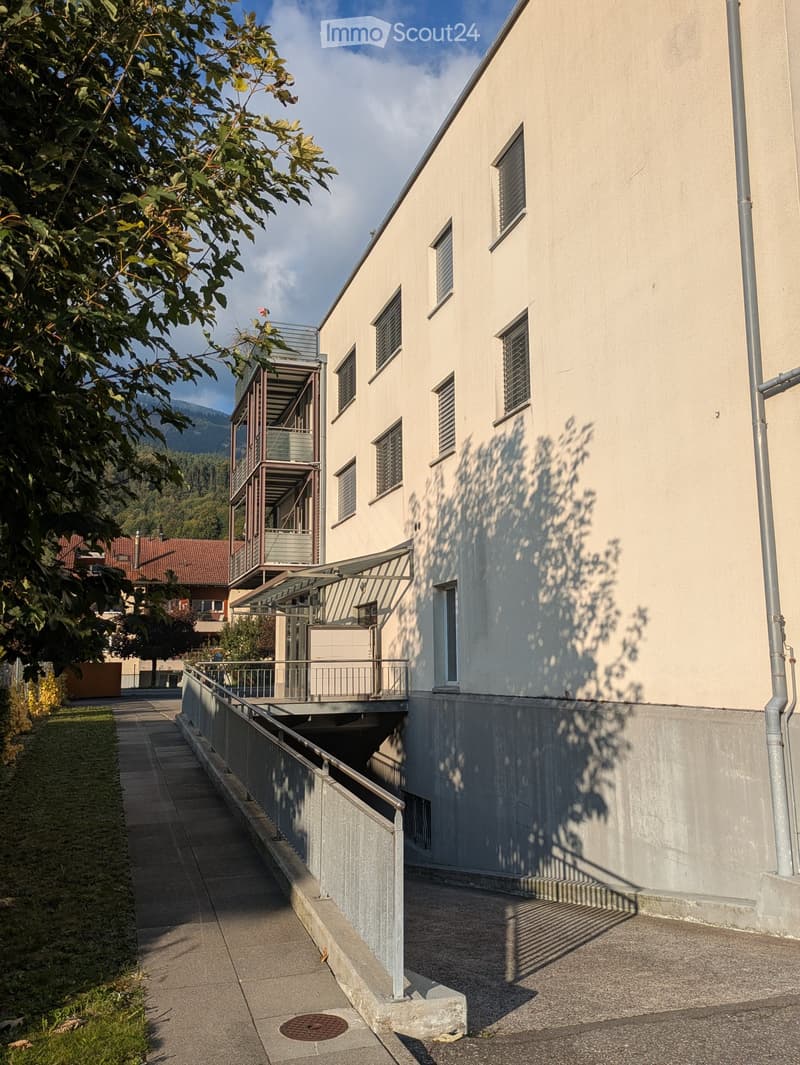 Concrete building with multiple floors, some balconies visible, and a pathway on the side