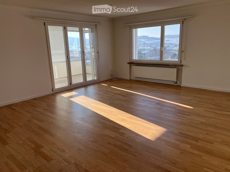Empty room with wooden flooring, large windows, and a sliding glass door leading to a balcony.