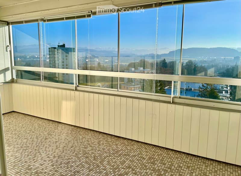 Empty room with large windows offering a scenic view of the city and mountains, featuring tiled flooring and light-colored paneling.