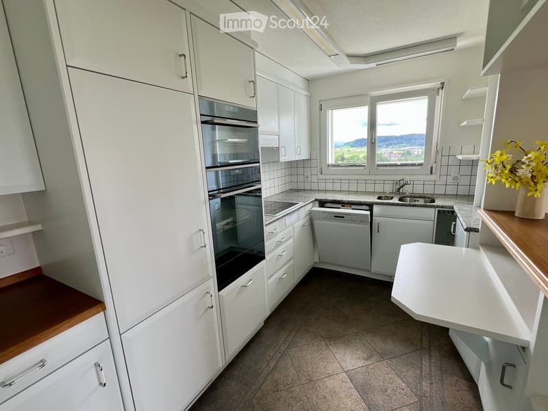 Modern kitchen with white cabinets, stainless steel appliances, and a large window offering a scenic view.