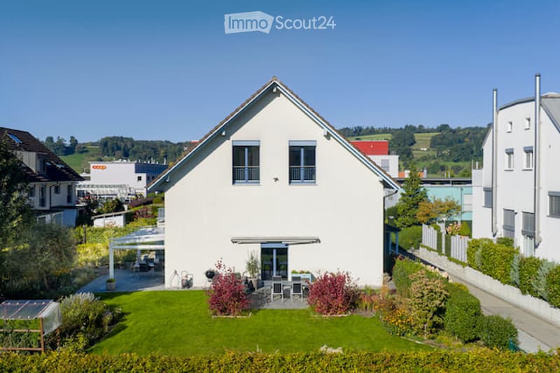 Single-family house with a modern design, white exterior, multiple windows, and a well-maintained garden with outdoor seating area.