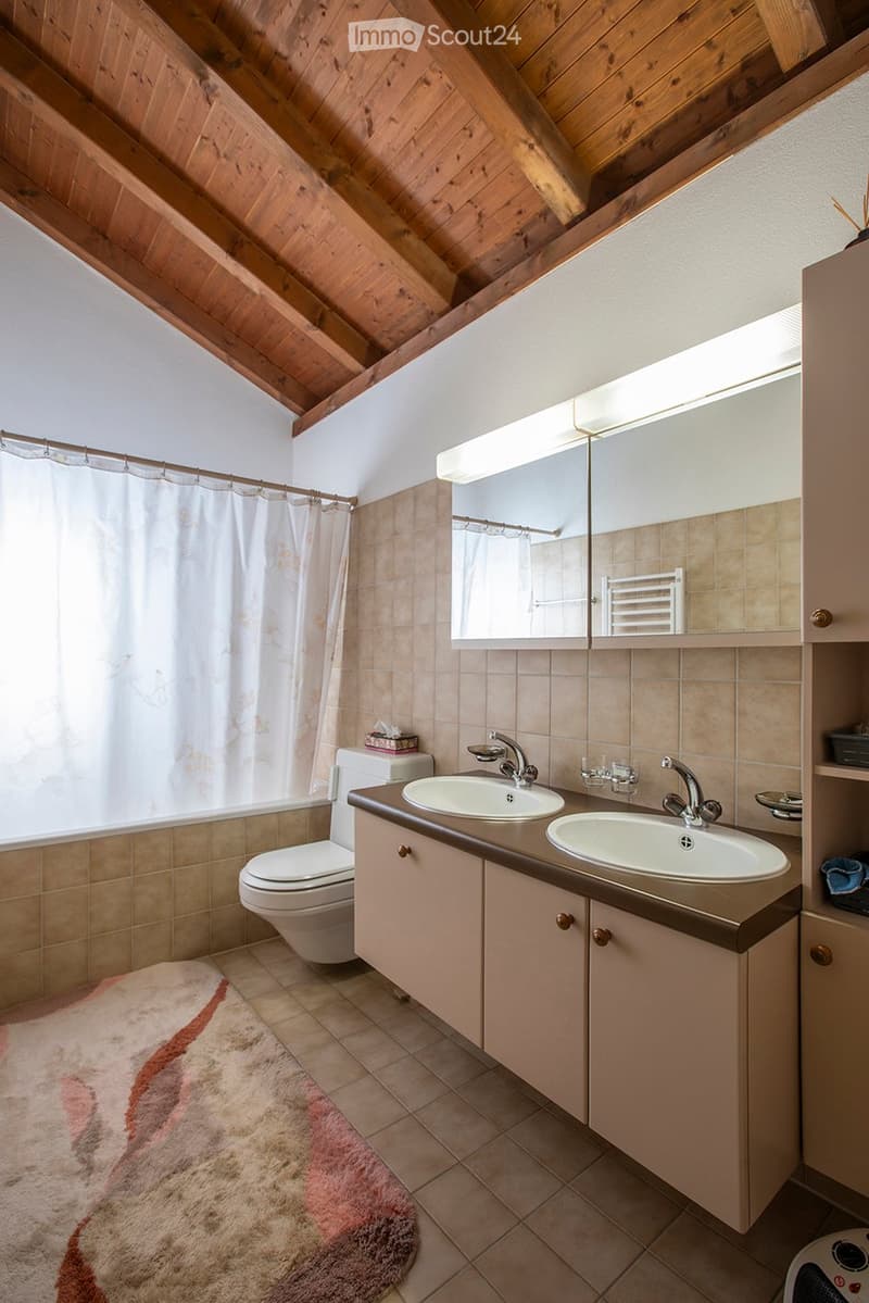 bathroom with beige tiles, wooden ceiling, sink with two faucets, toilet, two mirrors above sink, white shower curtain, floor mat