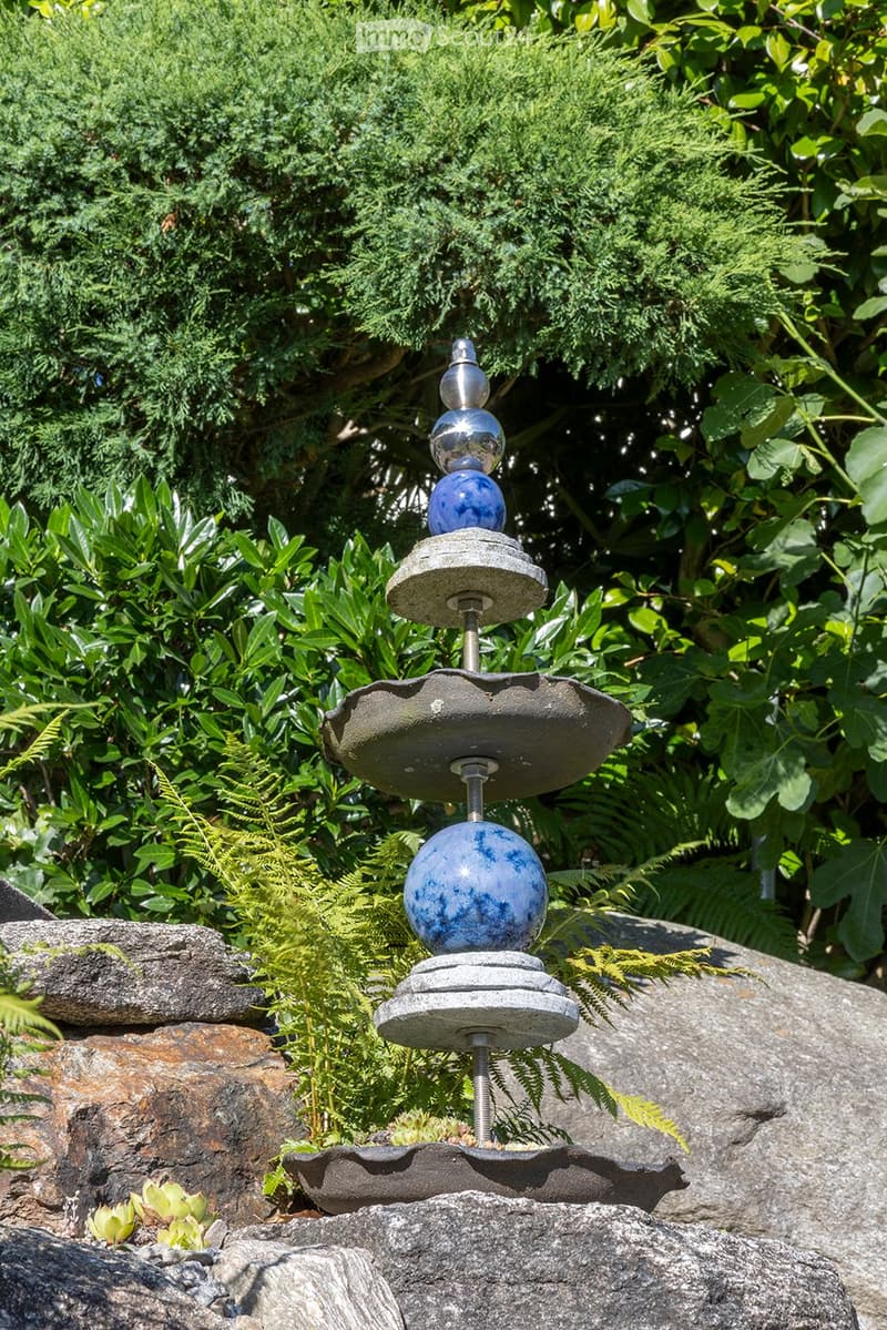 blue and silver sphere structure, grey cement bases, rocks, greenery