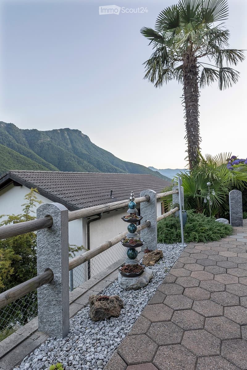 Wooden fence, rock garden, pathway, house in the background, mountains in the distance.