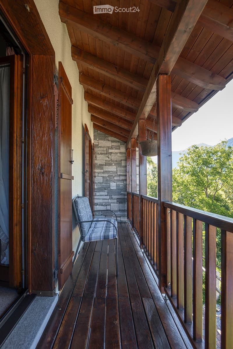 Wooden balcony with floor, wooden wall, railings, chair, hanging plant pot, view of trees and mountains