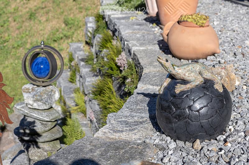 stone wall, green grass, brown clay pots with plants, brown sculpture of a frog, blue glass sphere