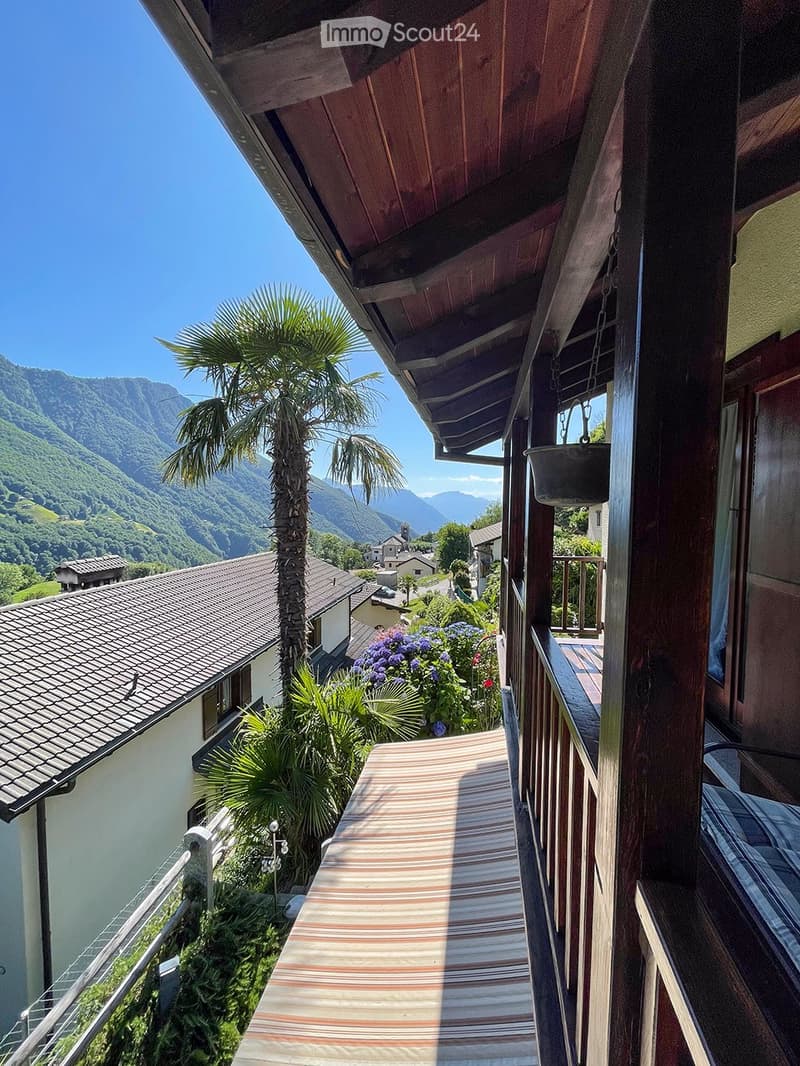 House with balcony, mountains in the background, wooden ceiling, flowers in the garden