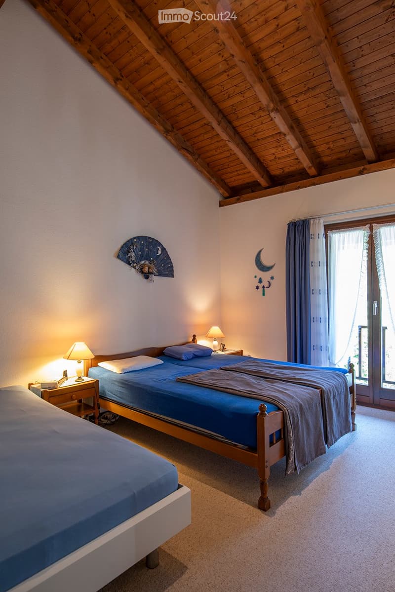 2 beds, blue bedding, nightstands with lamps, fan on wall, sliding glass door to balcony