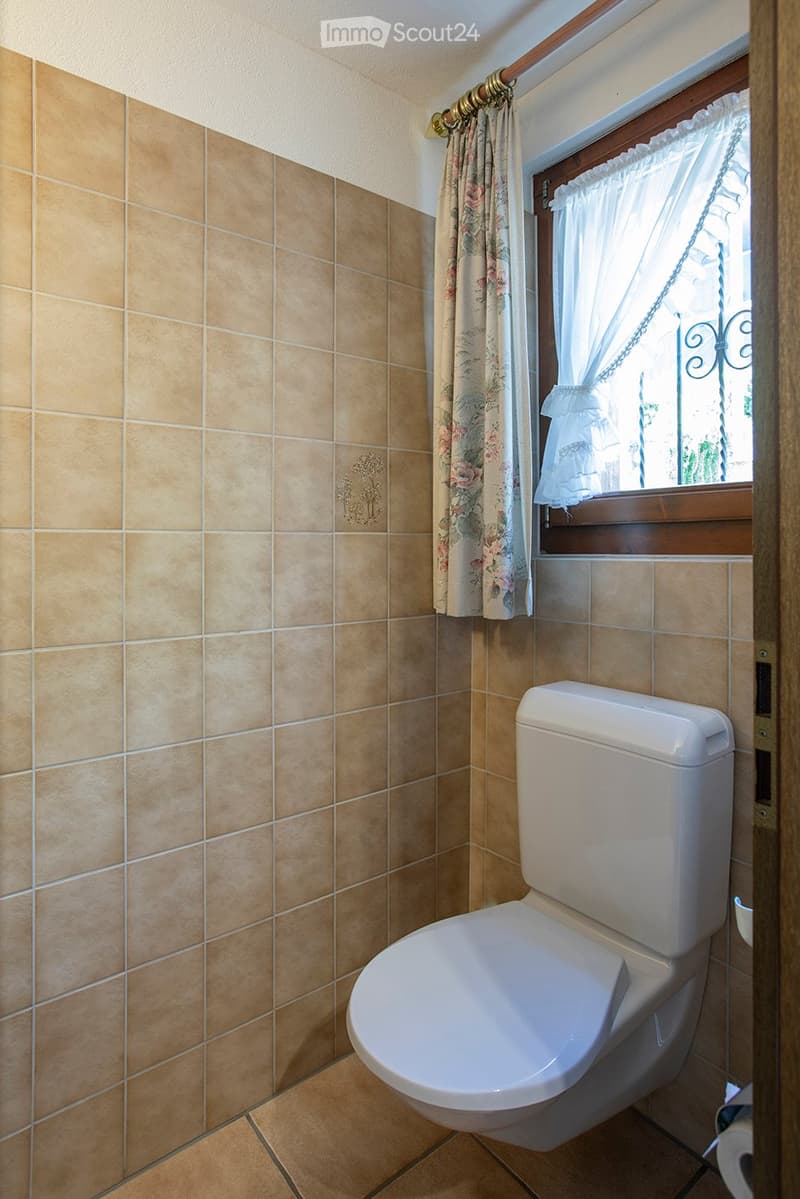A toilet in a corner of a room with tile walls and a window.