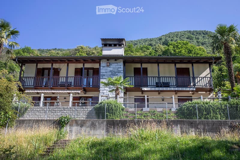 2 story house, balconies, trees, mountains in the background
