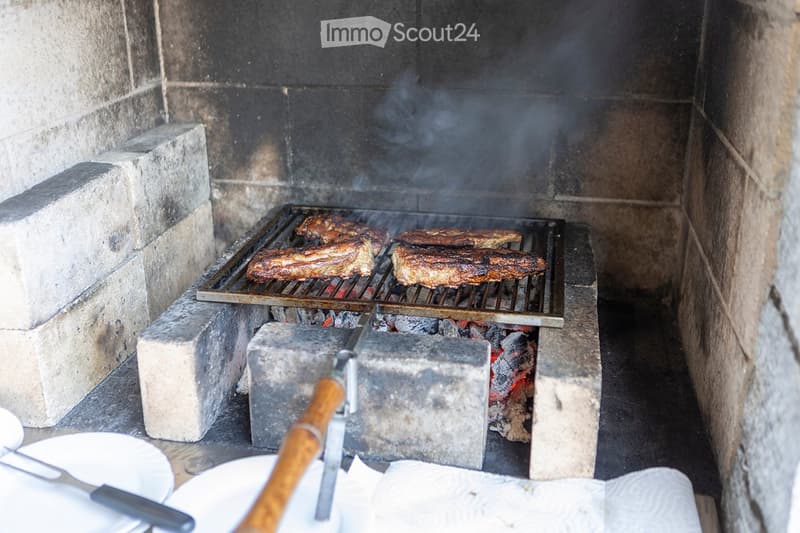 an outdoor cooking space with a grill and a fireplace, stone walls, plates and utensils on the ground
