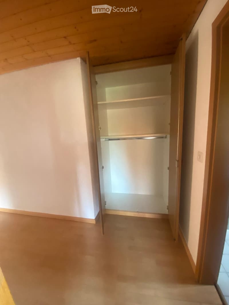 Empty hallway with wooden flooring, white walls, and an open closet with empty shelves and a hanging rod.