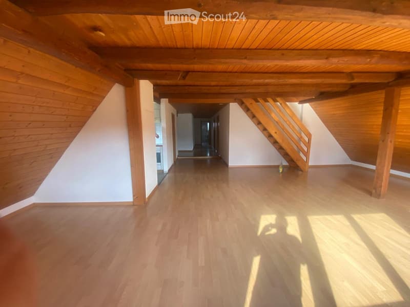 Empty attic space with wooden floors, exposed wooden beams, and a staircase leading to another area.