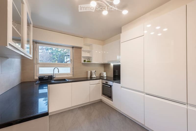 Kitchen. Modern kitchen with white cabinets, black countertop, stainless steel appliances, and a window overlooking a garden.