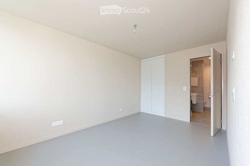 Empty room with light grey walls and floor, featuring a built-in closet and an open doorway leading to a bathroom.