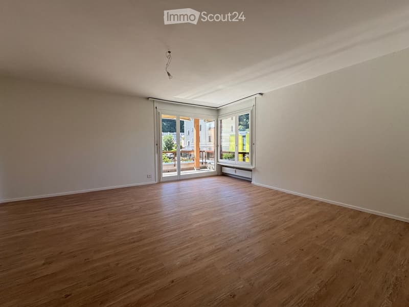 Empty room with wooden flooring, large windows, and sliding glass doors leading to a balcony.
